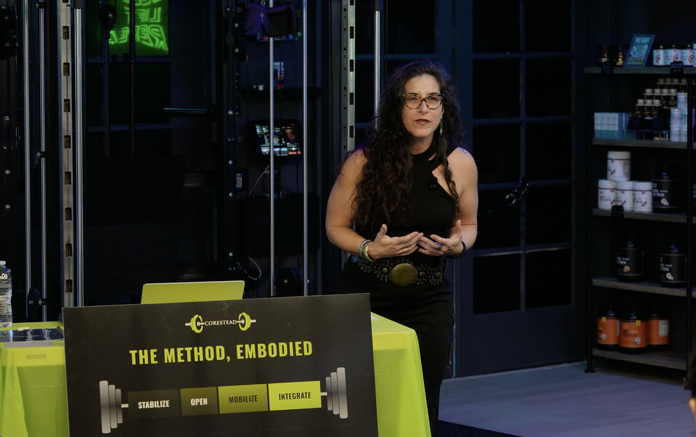 Emily Frydrych presenting at a Lifting From Within workshop, beside a lectern sign reading The Method, Embodied with the four phases listed below it: stabilize, open, mobilize, integrate.